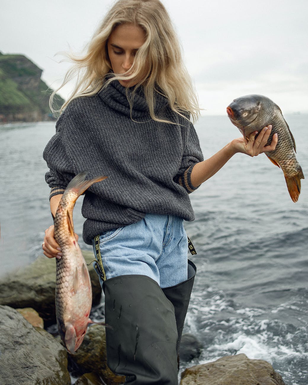 woman standing on a seashore holding two large fish in hands